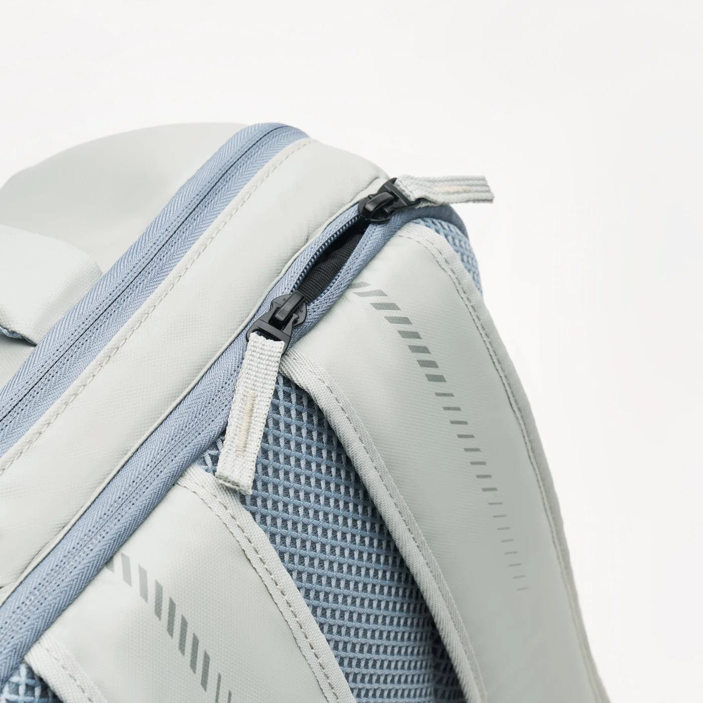 Close-up of the Kanso Intuko Tennis 23L Backpack in gray, featuring a mesh pocket, diagonal zipper, textured fabric, nylon straps, reflective print, and modern zipper pull. Its sleek design includes a handy racket compartment for added convenience.