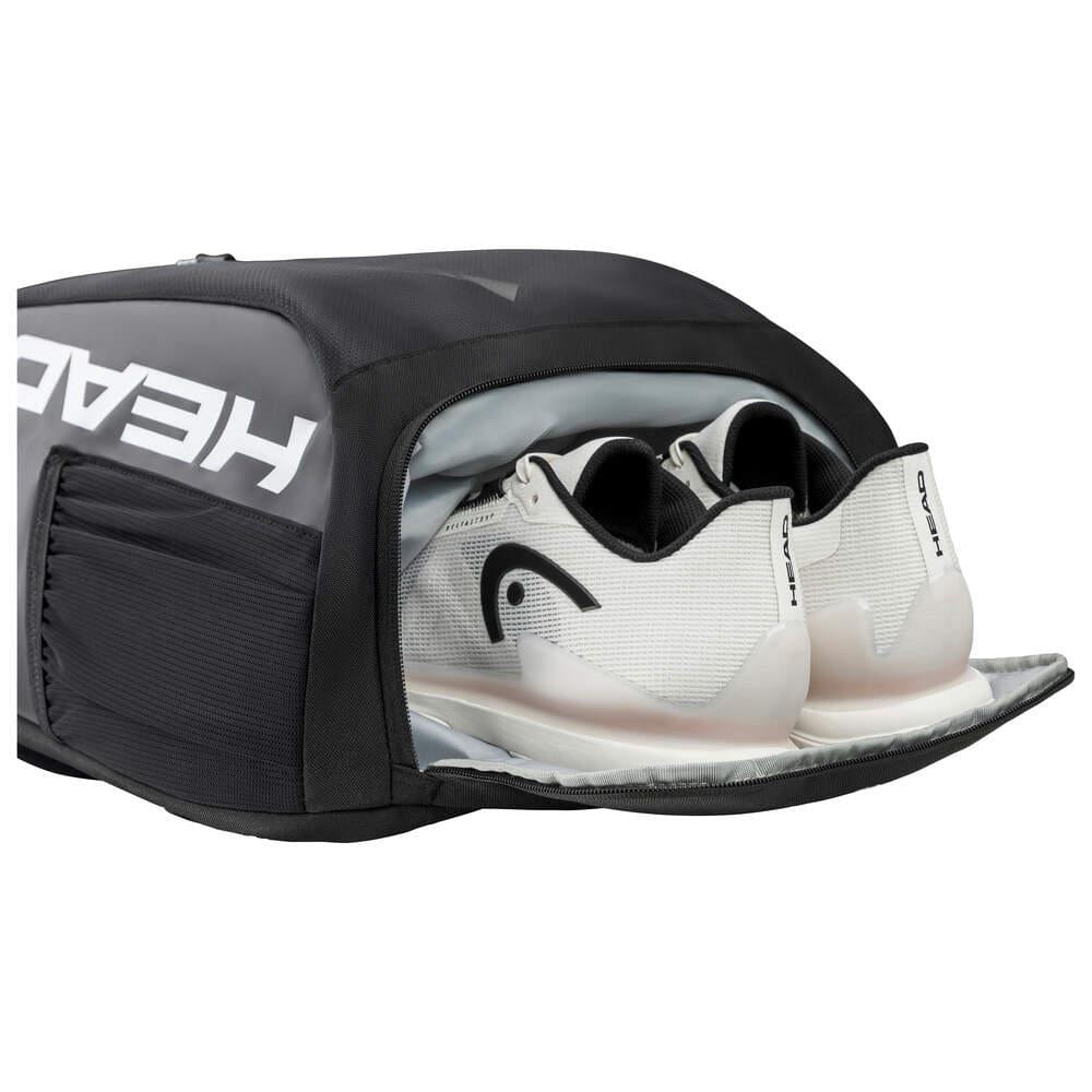 A HEAD Tour Tennis Backpack in Black/White is partially open, showcasing a pair of athletic shoes nestled within its spacious shoe compartment. The brand name "HEAD" is clearly visible on the side of the bag, indicating its racket compartment tailored for active athletes.