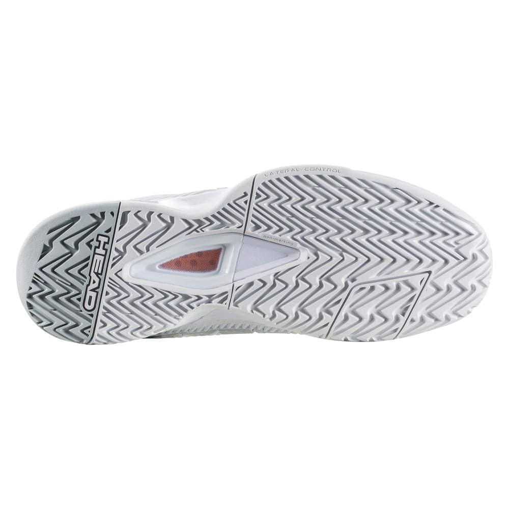 The image displays the sole of the HEAD Revolt Pro 4.0 Women's Tennis Shoes in white and grey, featuring a herringbone tread pattern known for its abrasion resistance. It also includes a transparent section showcasing a small red cushioned area, with the brand name "HEAD" displayed on the side.
