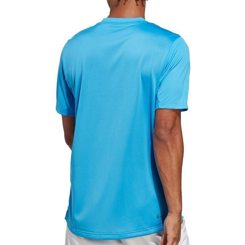 A person wearing a Pulse Blue ADIDAS Men's Club Tennis T-Shirt and white shorts is standing with their back facing the camera, showcasing the shirt's relaxed fit and subtle pattern. Designed with AEROREADY technology, it seamlessly combines style and functionality both on and off the court.