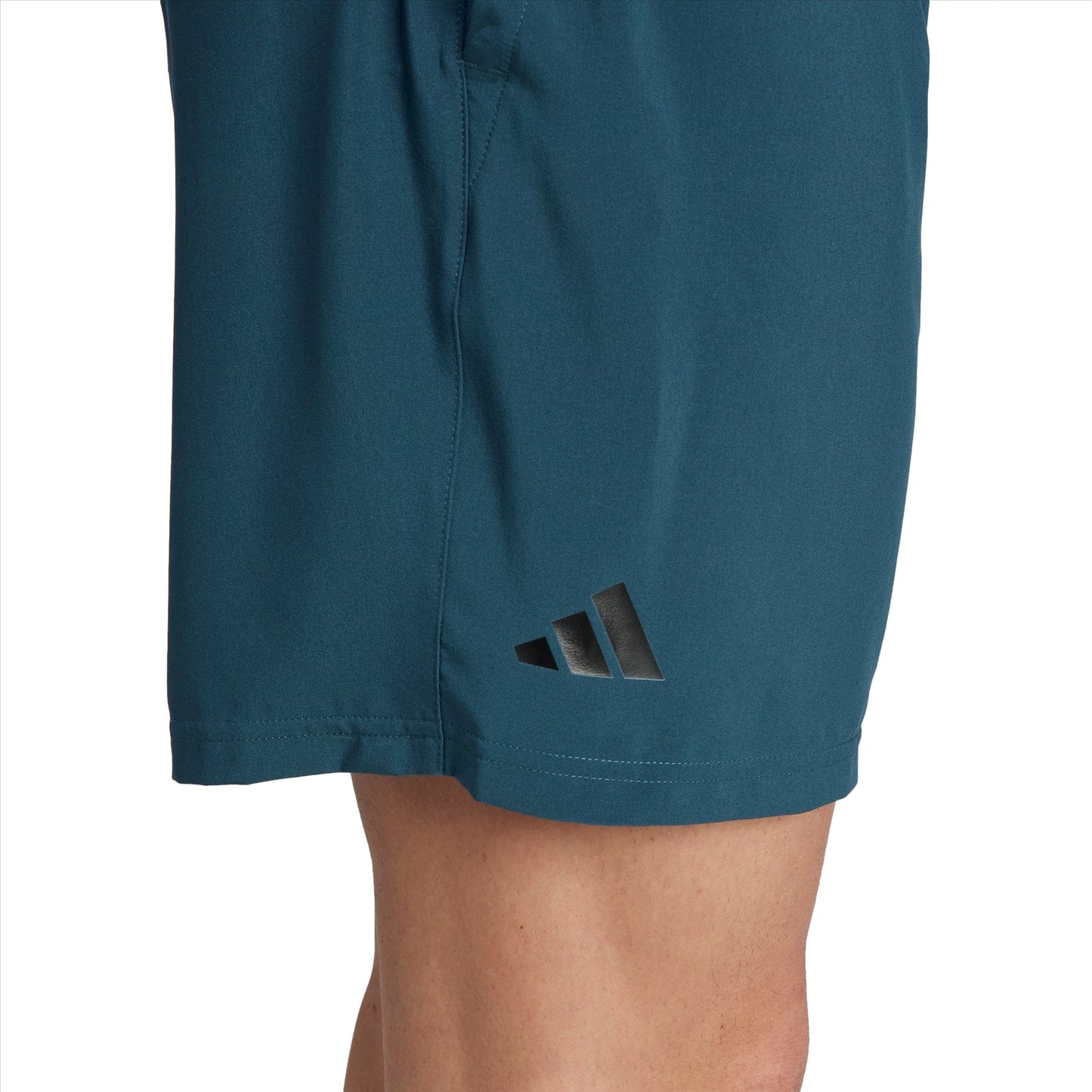 Close-up of an individual's leg in green adidas Club Stretch Woven 7" Men's Tennis Shorts, showcasing a black and white geometric logo near the hem. These shorts feature AEROREADY technology for optimal comfort, with a visible seam running down the side.