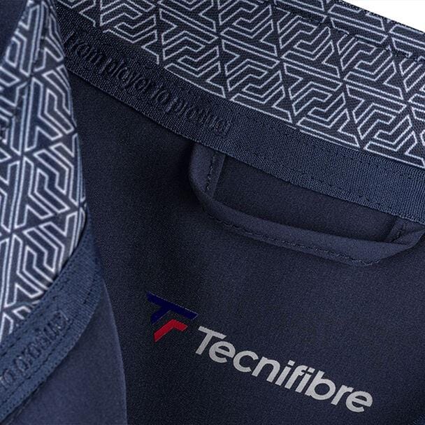 Close-up of the Tecnifibre Mens Light Tennis Jacket - Marine, highlighting its blue exterior with geometric pattern trim. The jacket boasts windproof and water-repellent fabric adorned with a red and blue stylized "T" logo, providing 4-way stretch for optimal comfort.