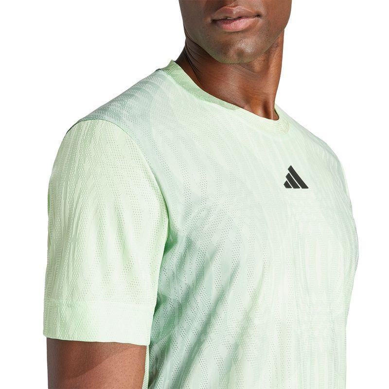 A person is wearing the ADIDAS Melbourne Men's Pro Tennis T-Shirt in a light green shade, featuring a subtle textured pattern and a small black logo on the chest. Crafted from recycled polyester with HEAT.RDY technology, this design emphasizes the upper torso and shirt styling.