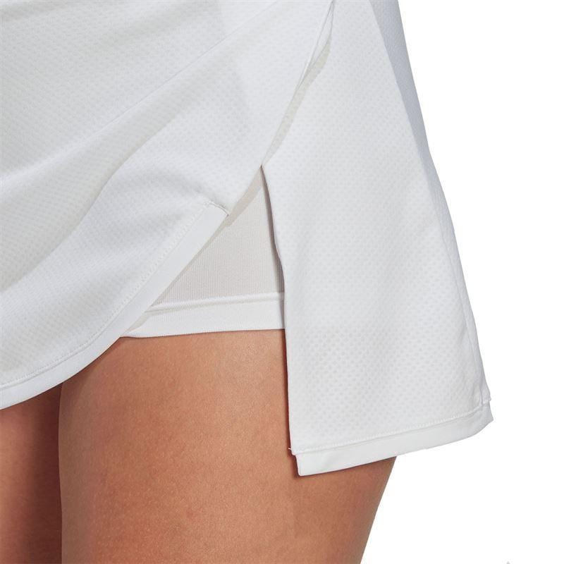 A close-up of a person wearing the ADIDAS Women's Club Tennis Skirt in white highlights its AEROREADY fabric texture and side slit. This lightweight, breathable material is ideal for sports, with an emphasis on the skirt's design, details, and wide waistband that ensures comfort during play.