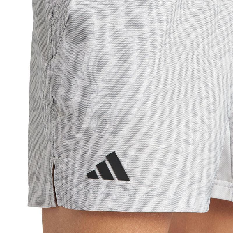 Close-up of a person wearing ADIDAS Melbourne Mens Pro 7 Inch Tennis Shorts in light gray, featuring an abstract wavy pattern. A black triangular adidas logo is prominently displayed on the recycled polyester fabric near the hem on the side. The shorts end slightly above the knee, highlighting their breathable HEAT.RDY technology against the person's skin.