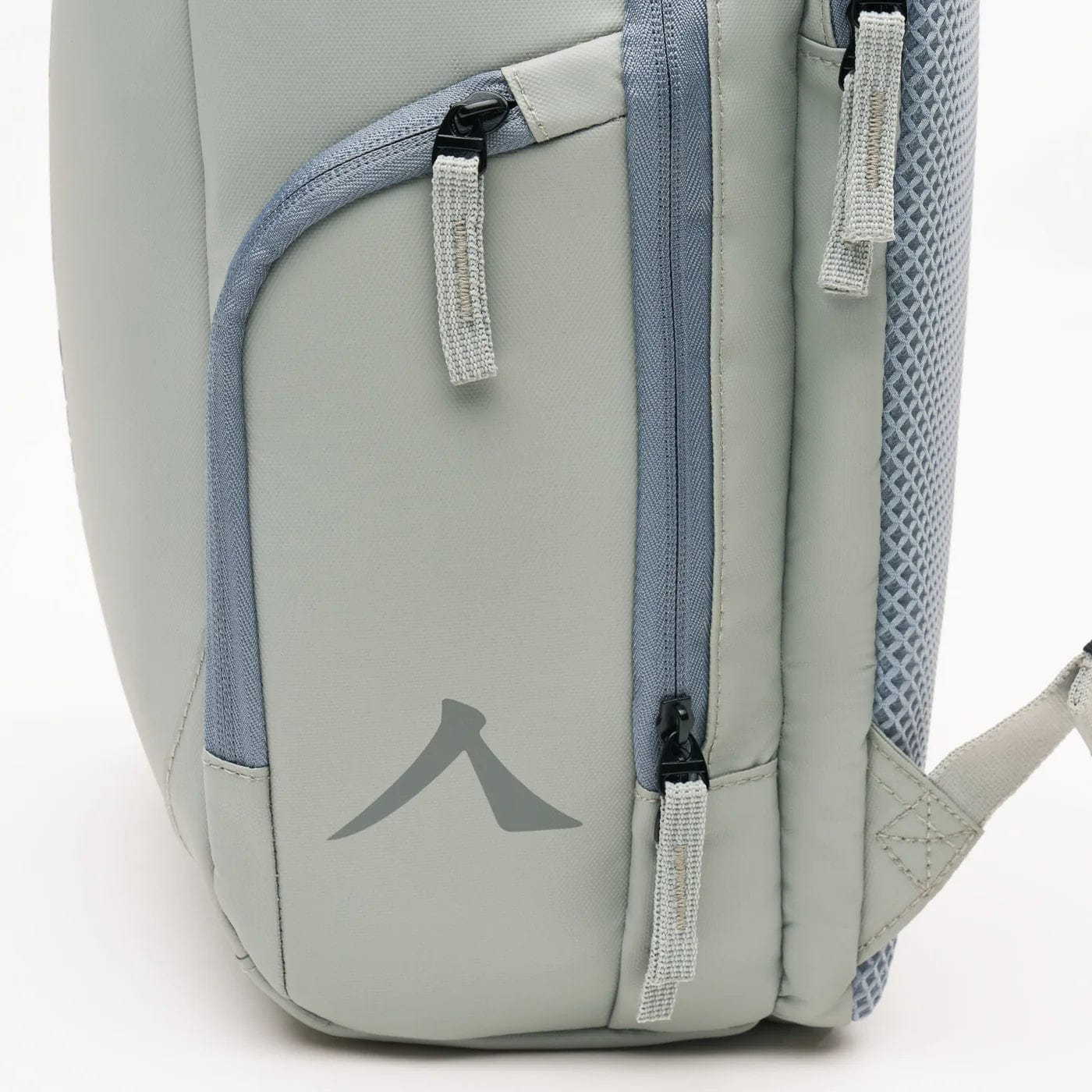 Close-up of the Kanso Intuko Tennis 23L Backpack in Grey, showcasing a side pocket with a gray zipper, stylized "A" logo, light blue accents, mesh back padding, and reflective print for safety.