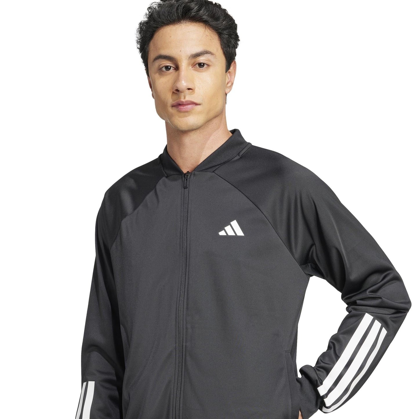 A person in an adidas Men's 3 Stripe Knit Tennis Jacket - Black, with a white chest logo and iconic stripes, stands with a neutral expression. The high-quality jacket features raglan sleeves and a full zipper.