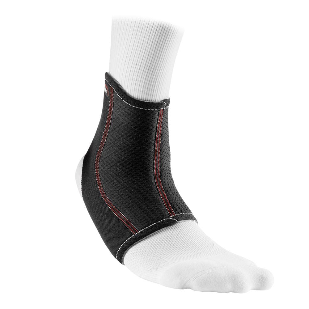A white socked foot wears the McDavid Ankle Sleeve from McDavid, a black neoprene ankle support brace with red stitching. This ankle sleeve covers the ankle and extends partially up the calf, providing effective compression therapy and support.