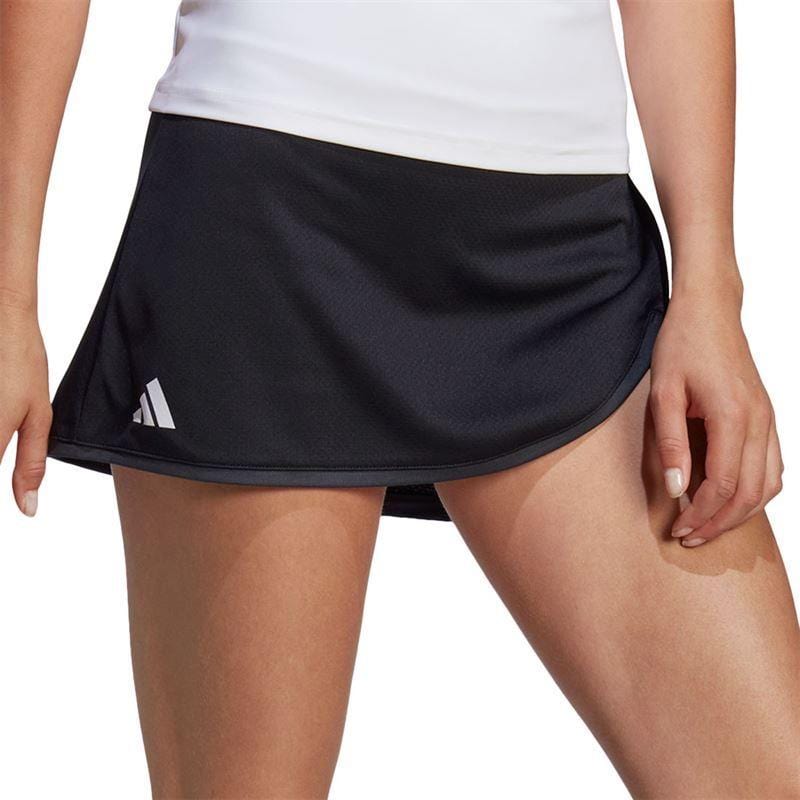 A person wearing a white top and the ADIDAS Women's Club Tennis Skirt in black, featuring a comfortable wide waistband and an adidas logo on the left side, stands confidently with one hand on their hip.