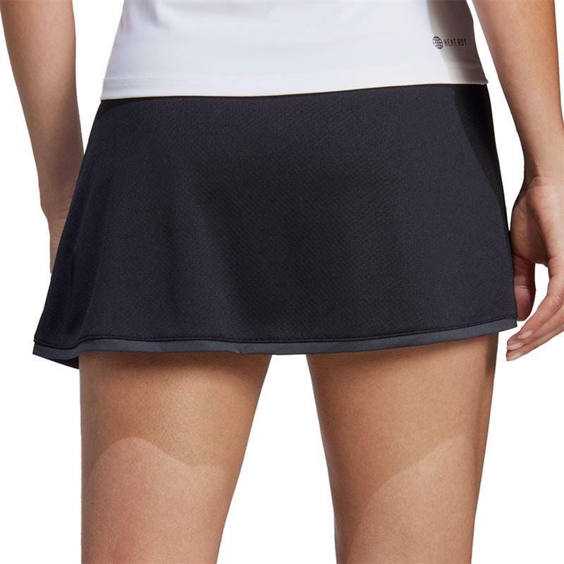 A person is depicted from behind wearing the ADIDAS Women's Club Tennis Skirt in black, featuring a comfortable wide waistband and paired with a white top. The slightly flared skirt is made of textured fabric and incorporates AEROREADY technology for improved breathability, set against a plain background.