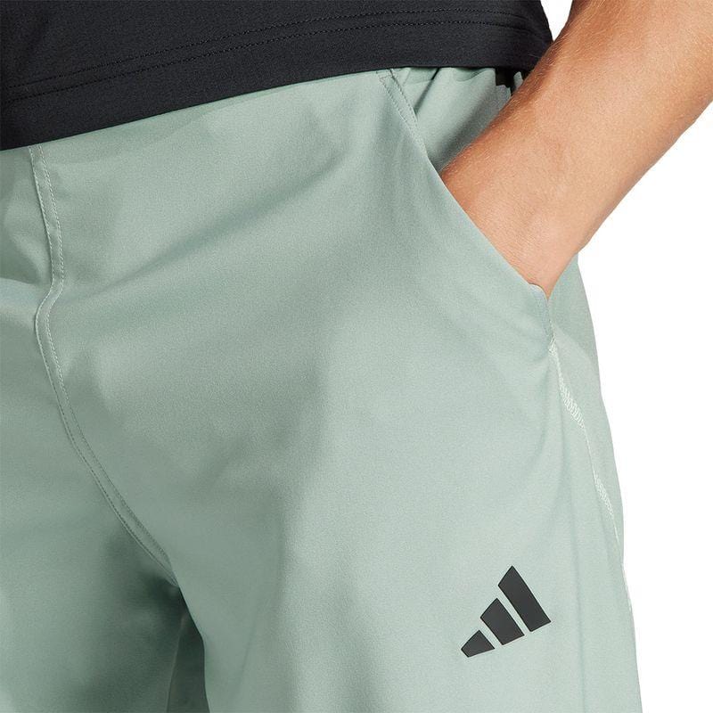 Close-up of a person wearing ADIDAS Melbourne Men's Pro Tennis Pants in green, featuring a discreet black adidas logo on the left side, designed with AEROREADY technology for increased comfort and breathability, with one hand casually resting in the pocket.