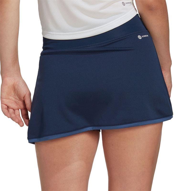A person is shown from the back wearing a navy blue ADIDAS Women's Club tennis skirt and a white top. The short, slightly flared skirt is perfect for any ADIDAS Club member.