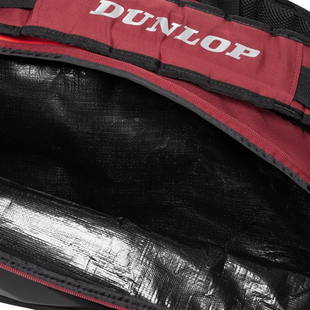 Close-up of an open Dunlop CX Performance 12 Tennis Racket Bag in black and red, showcasing the interior lining. The bag features a ventilated shoe compartment and prominently displays a red Dunlop logo on the top flap. Inside, it is lined with a shiny, black, water-resistant material for added protection.