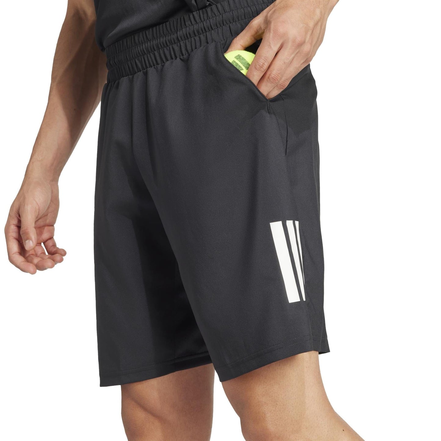 A person in adidas Men's 3 Stripe Tennis Shorts - Black, featuring a white logo, slides a yellow card into the pocket. These shorts offer an elastic waistband and moisture-wicking fabric, paired perfectly with a sleek black top.