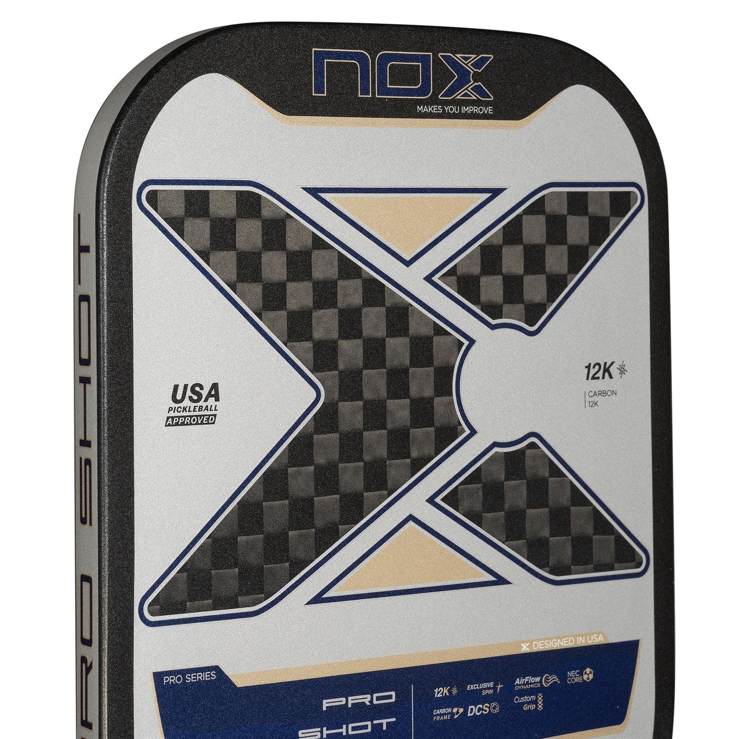 Close-up of the NOX Pro Shot Pickleball Paddle in black and blue, showcasing a bold checkered "X," "12K Carbon" label, and USA Pickleball Approved stamp on a sleek metallic and blue surface.