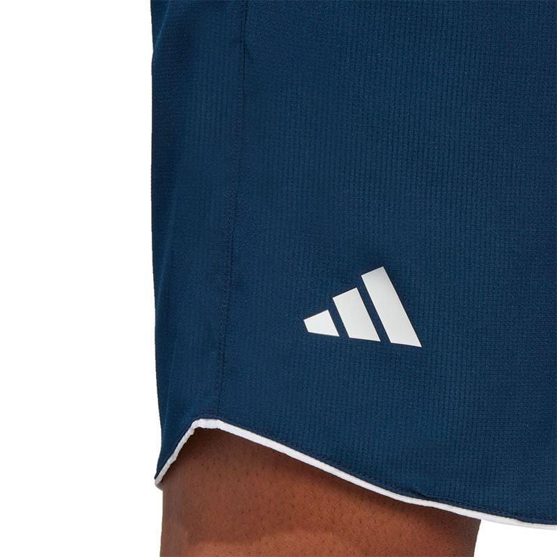 Close-up of a person wearing navy ADIDAS Mens Club 7" Tennis Shorts, showcasing a white logo near the hem. Made from lightweight ripstop fabric, these shorts incorporate AEROREADY technology and are accented with white piping along the edges for a sleek look.