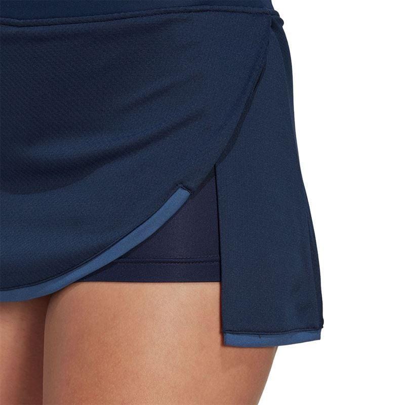 A close-up of a person wearing the ADIDAS Women's Club Tennis Skirt in navy emphasizes its layered structure, complete with a side slit that reveals the AEROREADY sports shorts beneath. The smooth, lightweight fabric makes this skirt ideal for the tennis court.