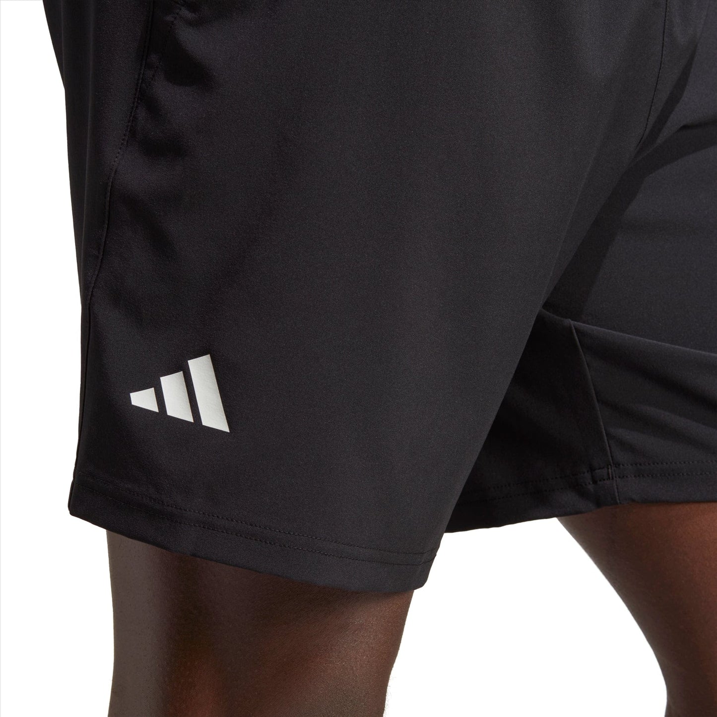 Close-up of an individual wearing the adidas Club Stretch Woven 7" Men's Tennis Shorts in black, featuring a white Adidas logo on the left thigh. The smooth fabric, enhanced with AEROREADY technology, provides a sleek and fitted appearance against a crisp white backdrop.