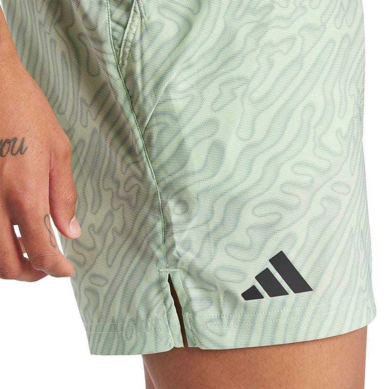 A person is wearing light green ADIDAS Melbourne Men's Pro 7 Inch Tennis Shorts featuring a wavy pattern and the iconic black Adidas logo. Constructed from recycled polyester, these shorts keep you cool with HEAT.RDY technology. A part of their hand is visible, revealing a wrist tattoo with the word "you.