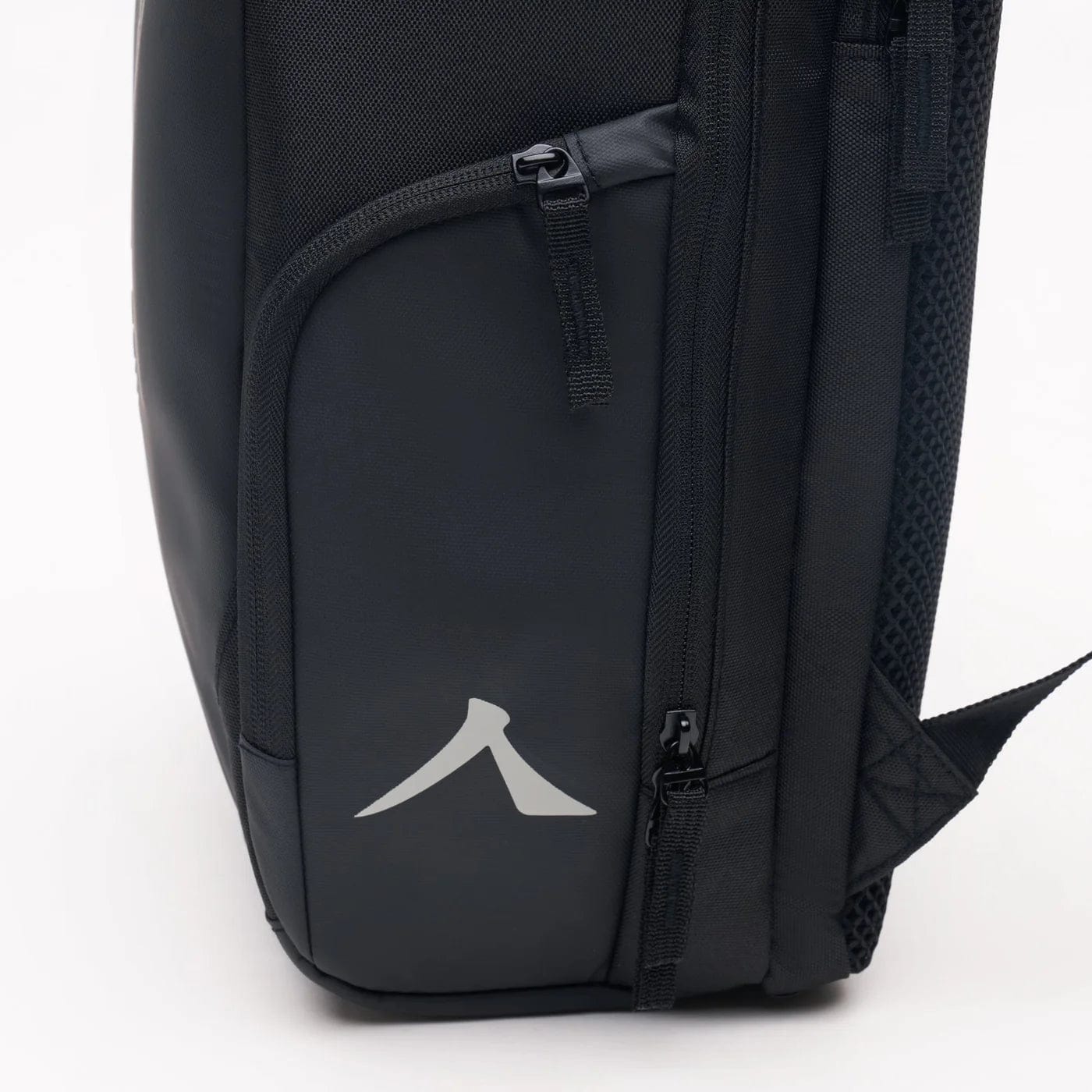 Meet the Kanso Intuko Tennis 23L Backpack in Black: featuring a sleek glossy panel with a minimalist gray arrow logo. Designed for everyday use, it has two visible zippers—a top horizontal and a side vertical—providing easy access to separate compartments for simple organization.