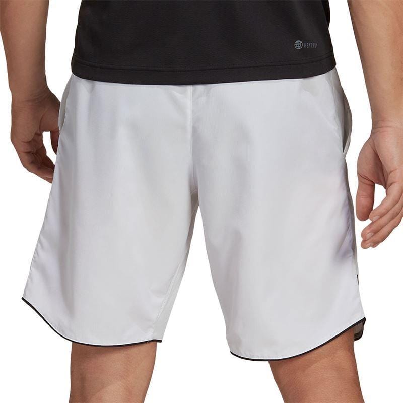 A person is wearing a black shirt and ADIDAS Men's Club 7" Tennis Shorts in white, crafted from AEROREADY ripstop fabric, standing with hands by their sides. The background is plain and unobtrusive.