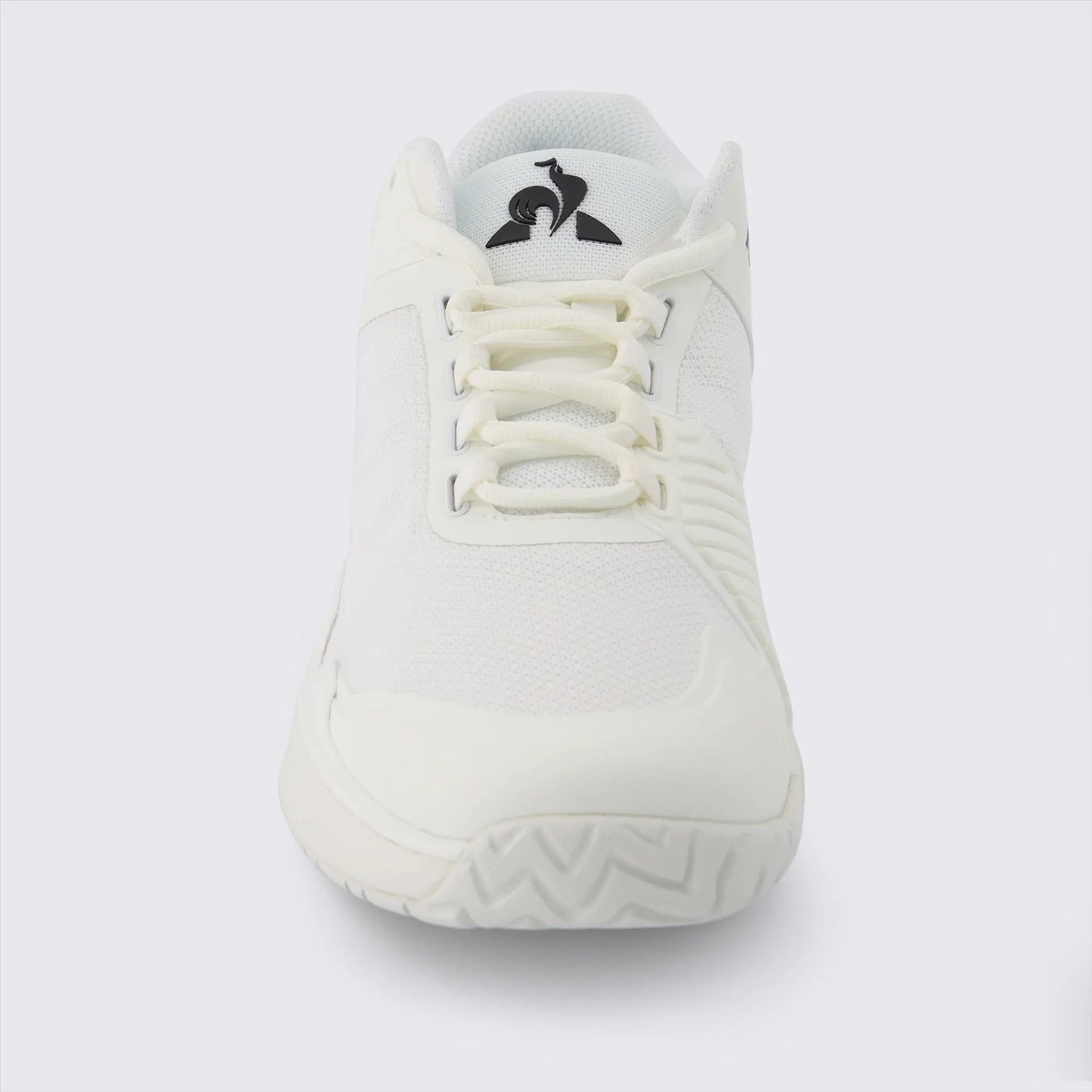 The Le Coq Sportif Futur LCS T01 All Court Tennis Shoes in white are showcased in a front view, highlighting a stylized penguin logo on the tongue. This sneaker, designed by Le Coq Sportif, features a breathable mesh upper and a Comfort EVA sole. Its textured design and minimalist style stand out against a plain white background.