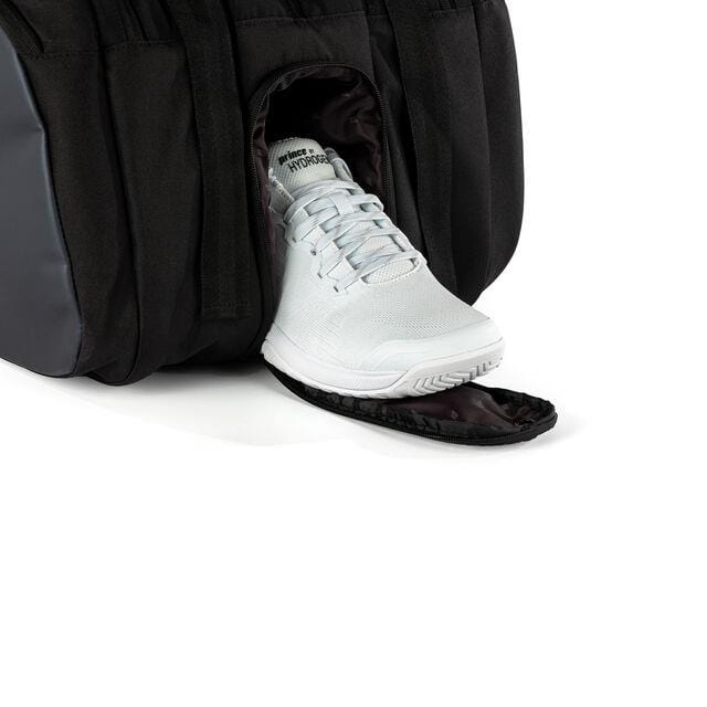 A stylish black Prince Tour 3 Comp 12 Racket Tennis Bag, featuring a specialized shoe compartment to keep items organized, reveals a white sneaker partially pulled out.