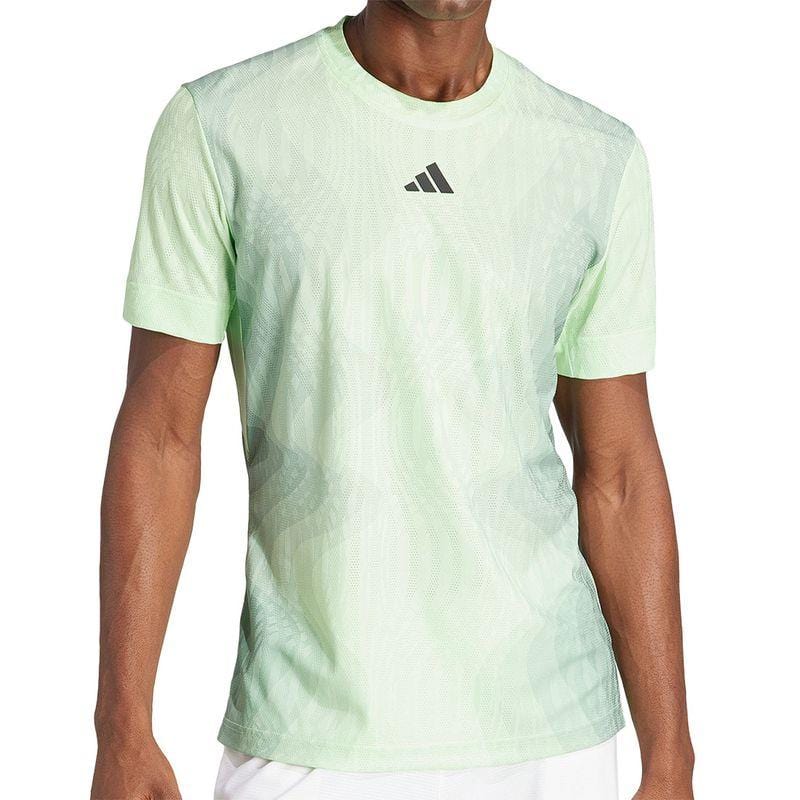 The image shows someone wearing a green ADIDAS Melbourne Men's Pro Tennis T-Shirt by adidas, showcasing an abstract pattern and a subtle logo. Made from recycled polyester for sustainability, it guarantees comfort. The focus is also on their white shorts, emphasizing the torso and upper legs.