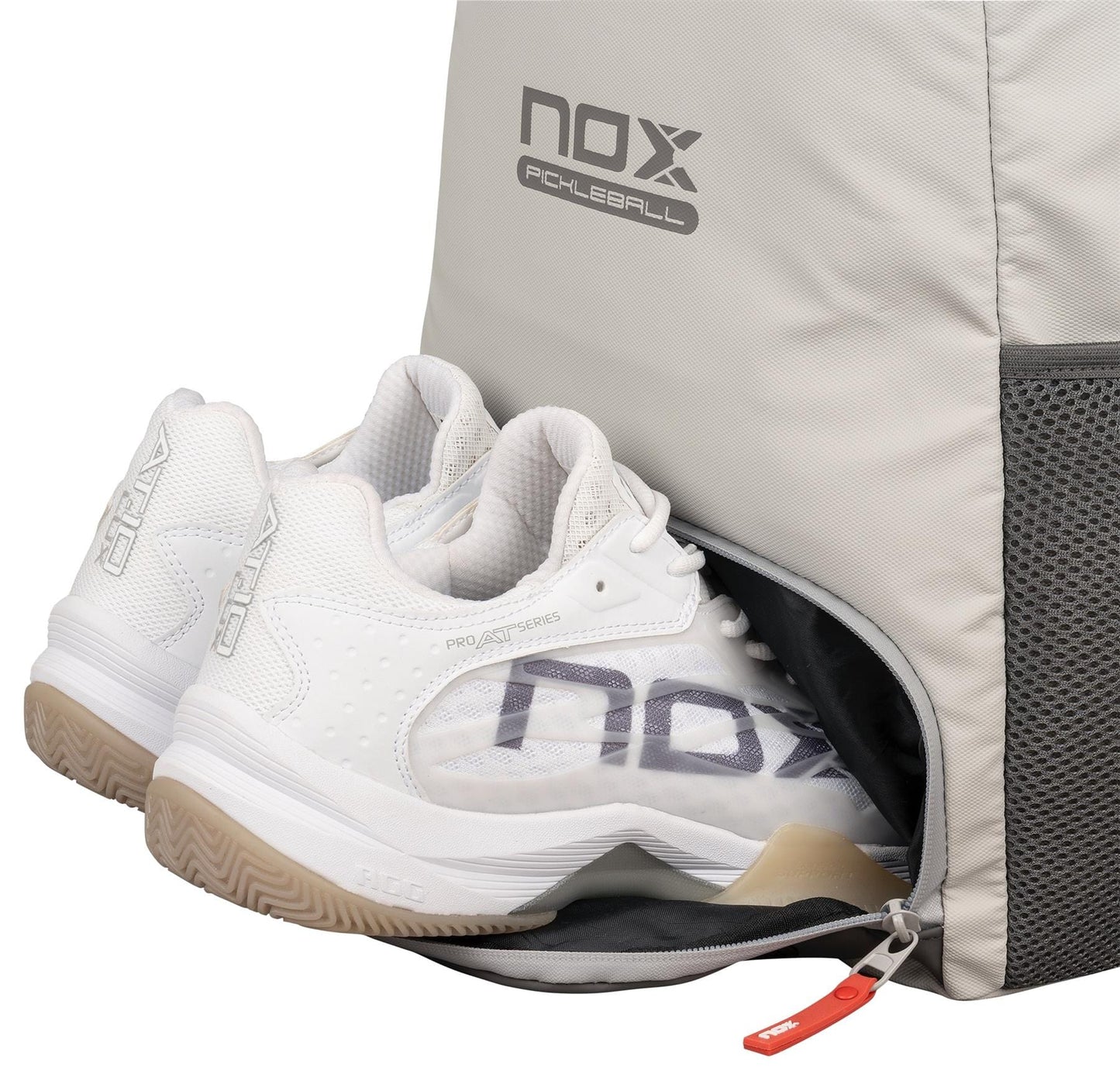 A pair of white athletic shoes partially inside a side compartment of the NOX Supra Pickleball Backpack - Cream, featuring ergonomic padded straps, a mesh pocket, and a visible zipper pull.