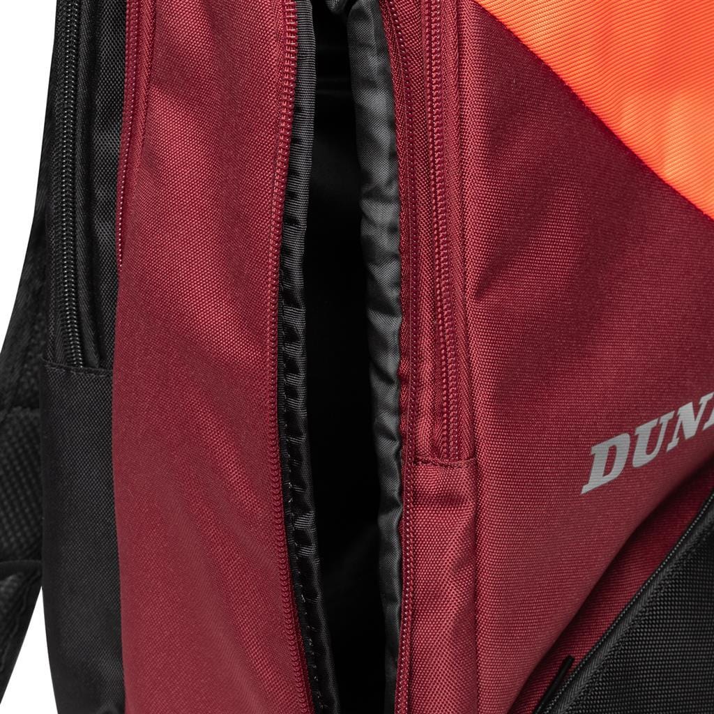 A close-up of the Dunlop CX Performance Tennis Backpack in black and red, showcasing its partially open zipper. The Dunlop brand name is partly visible on the right side in white lettering. The textured fabric includes an orange accent near the top, making it perfect for stylishly carrying rackets.