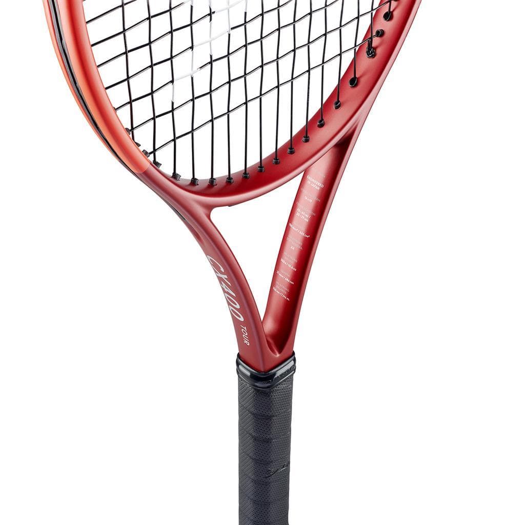 Close-up of a Dunlop CX 400 Tour 2024 Tennis Racket in red, showcasing the strings and part of the frame. The textured black grip enhances handling and the overall feel of the racket. Although there is text on the frame, it remains unreadable. Set against a plain white background, its potential for spin is emphasized.