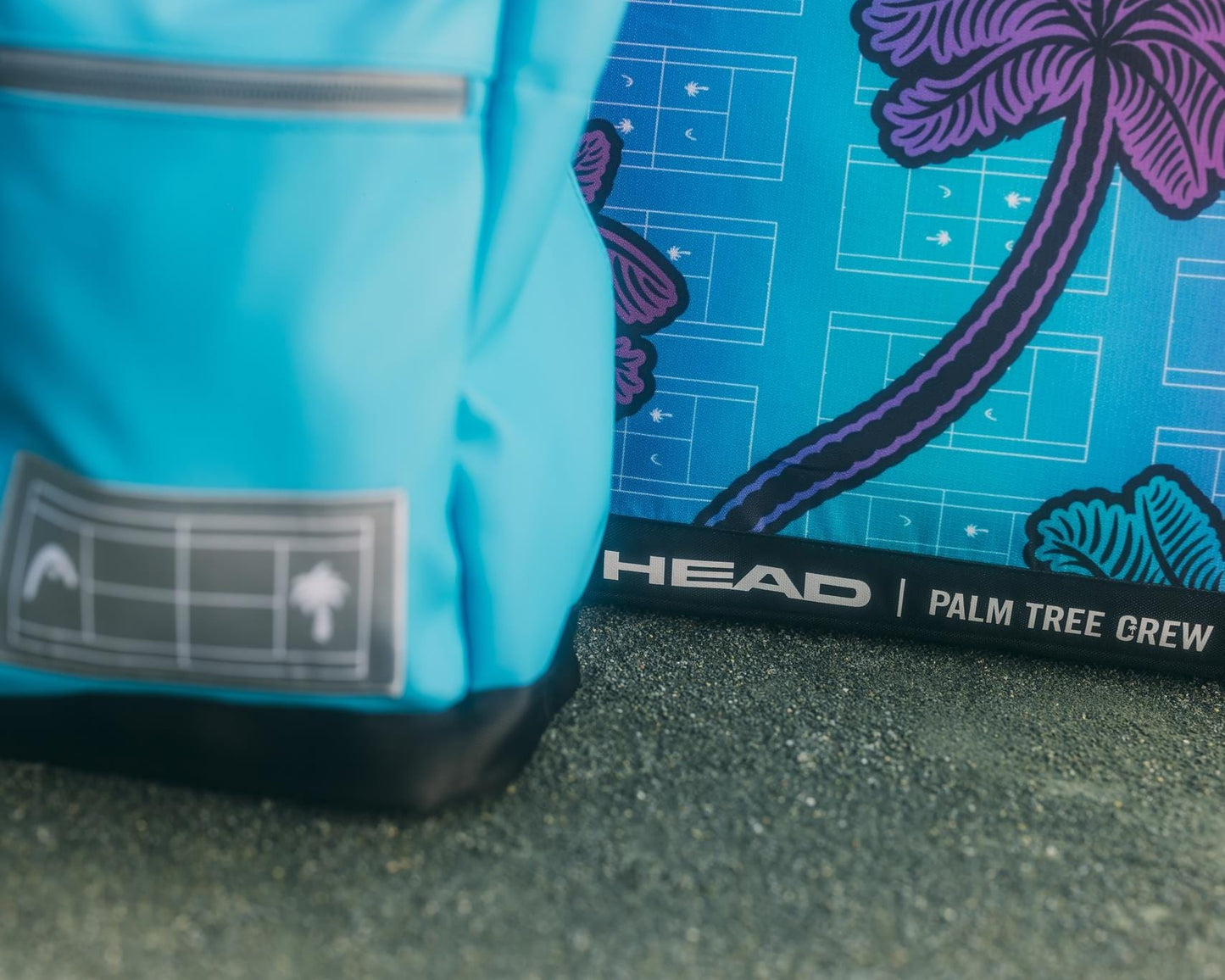 A close-up of the HEAD Tour Tennis Duffle Bag L - Palm Tree Crew next to a vibrant blue and purple item with palm tree graphics and "HEAD | PALM TREE CREW" printed near the bottom, both resting on a textured surface.