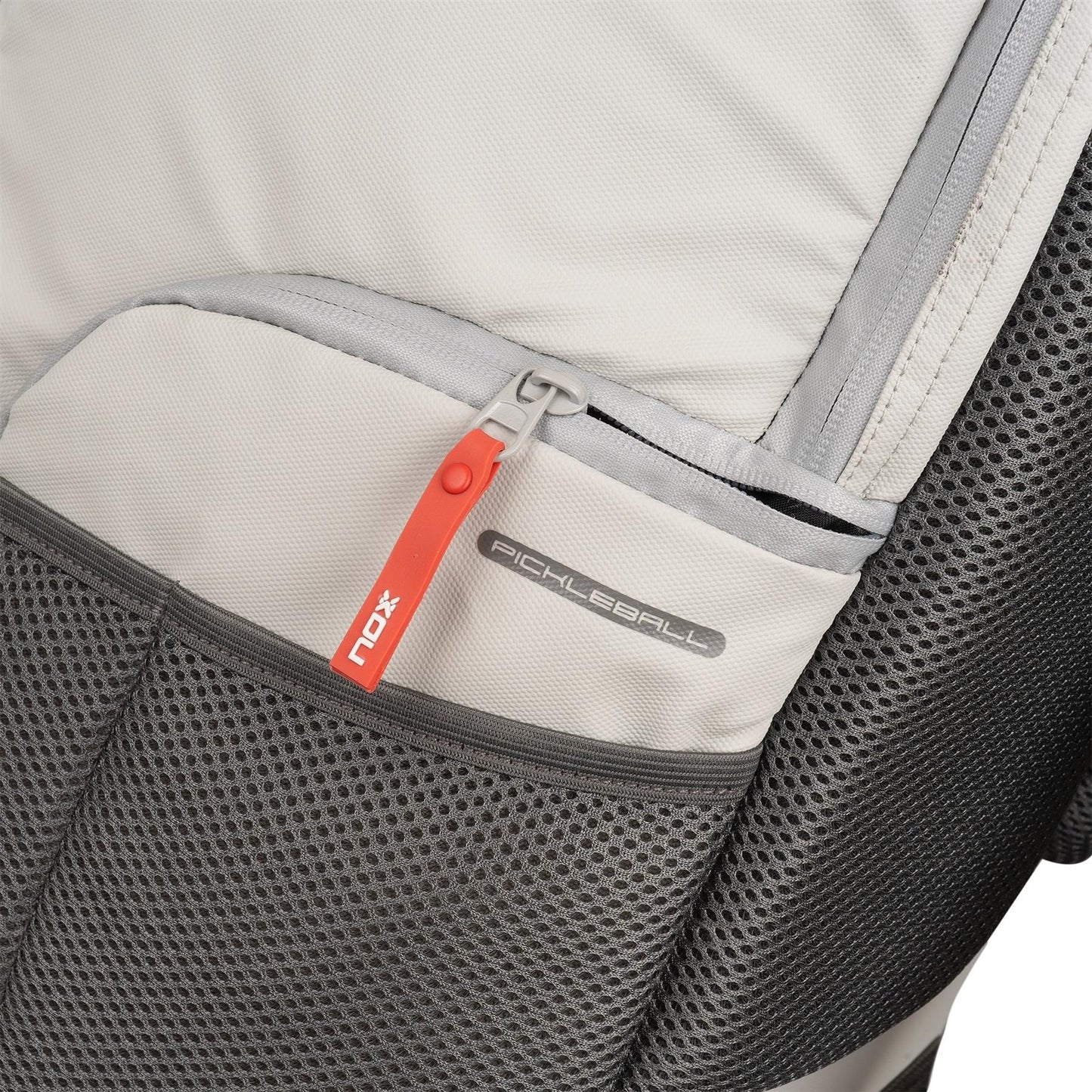 Close-up of the NOX Supra Pickleball Backpack in Cream, showing a red zipper pull with "NOX" branding and a "Pickleball" tag; features include mesh and fabric textures plus ergonomic padded straps for comfort.