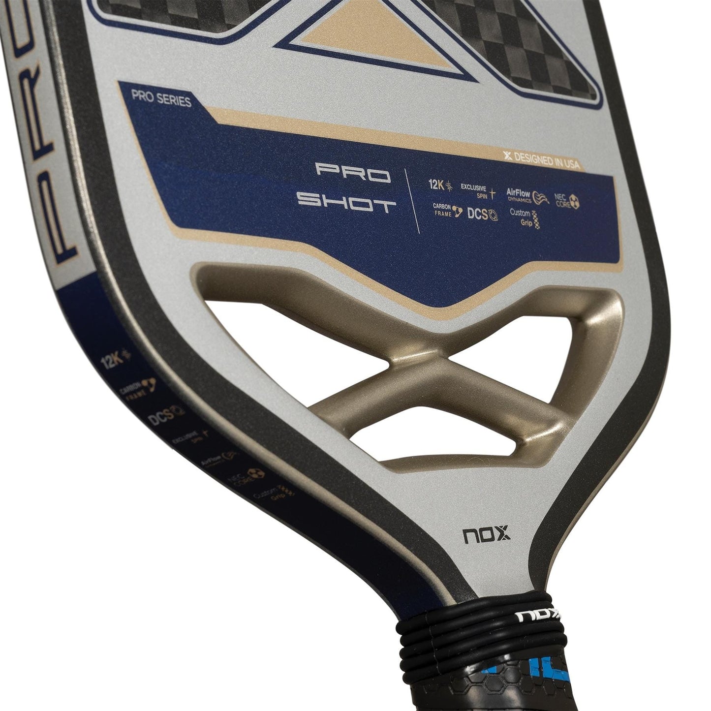 Close-up of the NOX Pro Shot Pickleball Paddle - Black / Blue by NOX, featuring a blue, black, and gold geometric design with visible branding and technical details on its 12K carbon fibre face and handle.