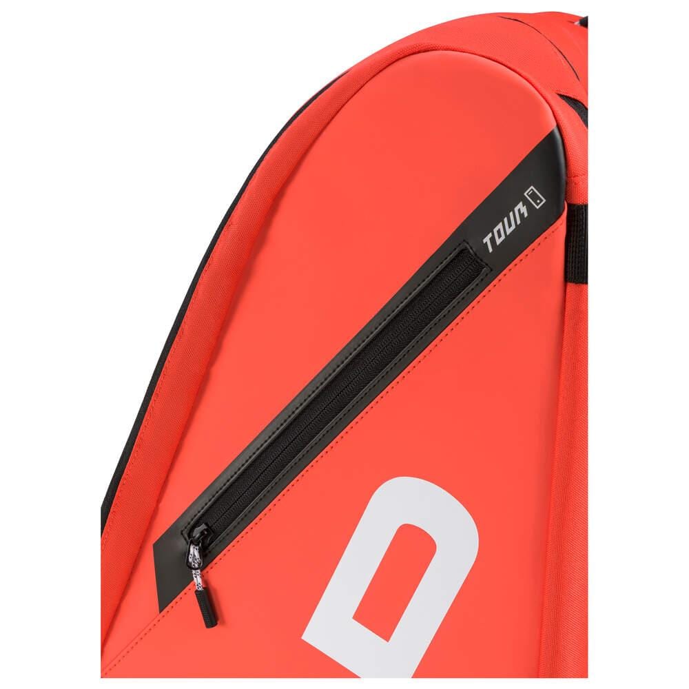 A close-up of the HEAD Tour Tennis Racket Bag XL in fluorescent orange showcases its sleek design, featuring a diagonal black zipper pocket marked "TOUR." The bag's smooth surface reveals part of a stylish white logo and offers a convenient backpack carry system for easy transport.