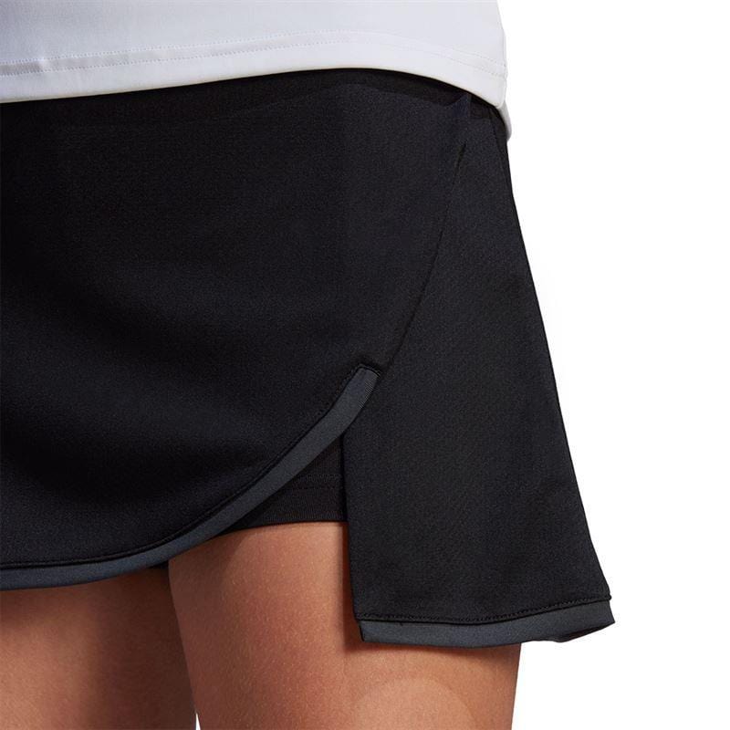 Close-up of a person wearing the ADIDAS Women's Club Tennis Skirt in black by adidas, standing against a plain background. Featuring a wrap design and advanced AEROREADY technology, the skirt effortlessly complements the visible white top and offers a comfortable wide waistband.