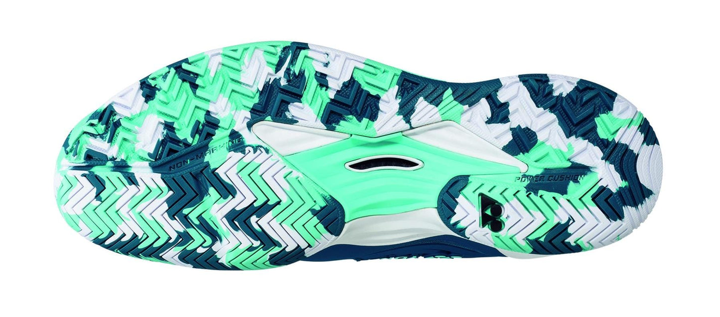 The image highlights the sole of the Yonex Power Cushion FusionRev 5 Men's Tennis Shoes in blue and green, displaying a herringbone tread pattern with colors such as green, teal, white, and dark blue. Engineered for traction, it integrates rubber and textured surfaces with a TPU Shank alongside Yonex FusionRev 5 technology for enhanced stability.