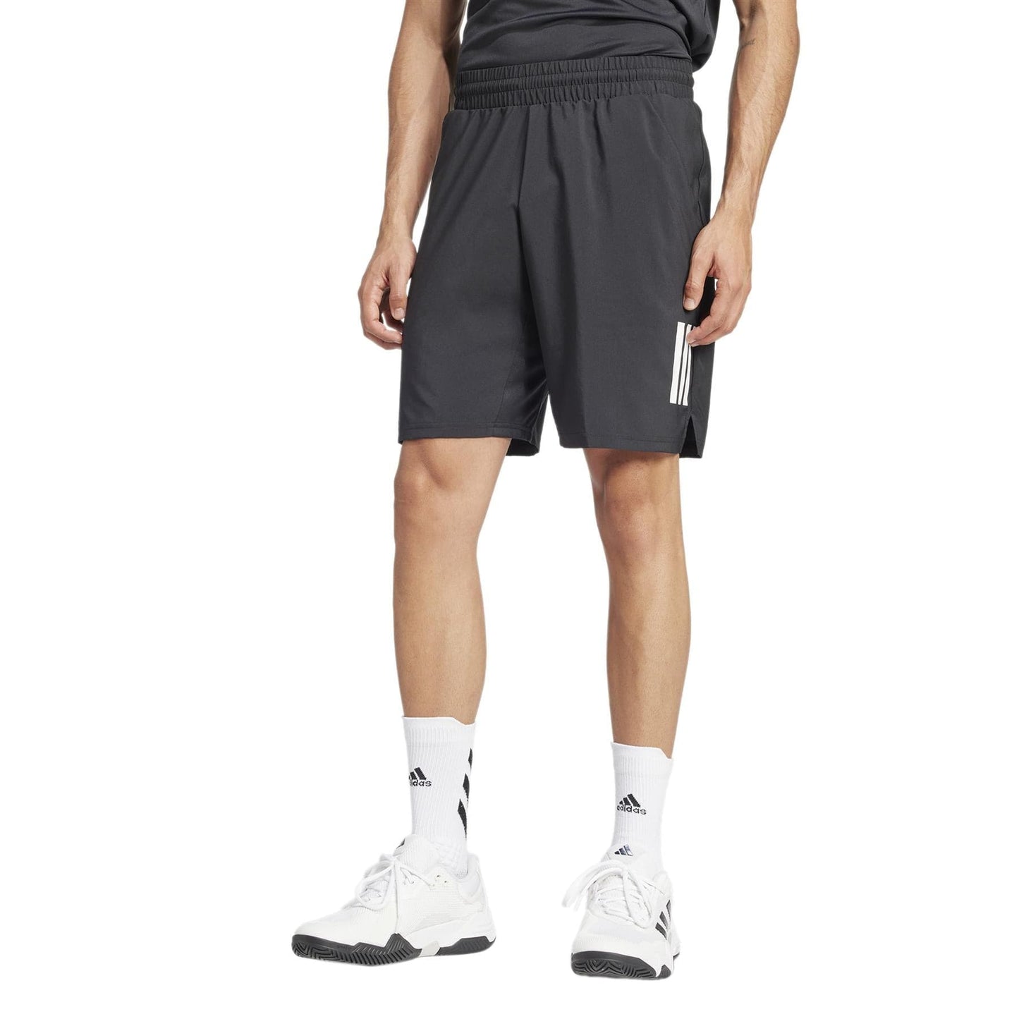 Against a plain white backdrop, a person sports moisture-wicking ADIDAS Men's 3 Stripe Tennis Shorts in black with an elastic waistband, paired with white socks and sneakers.
