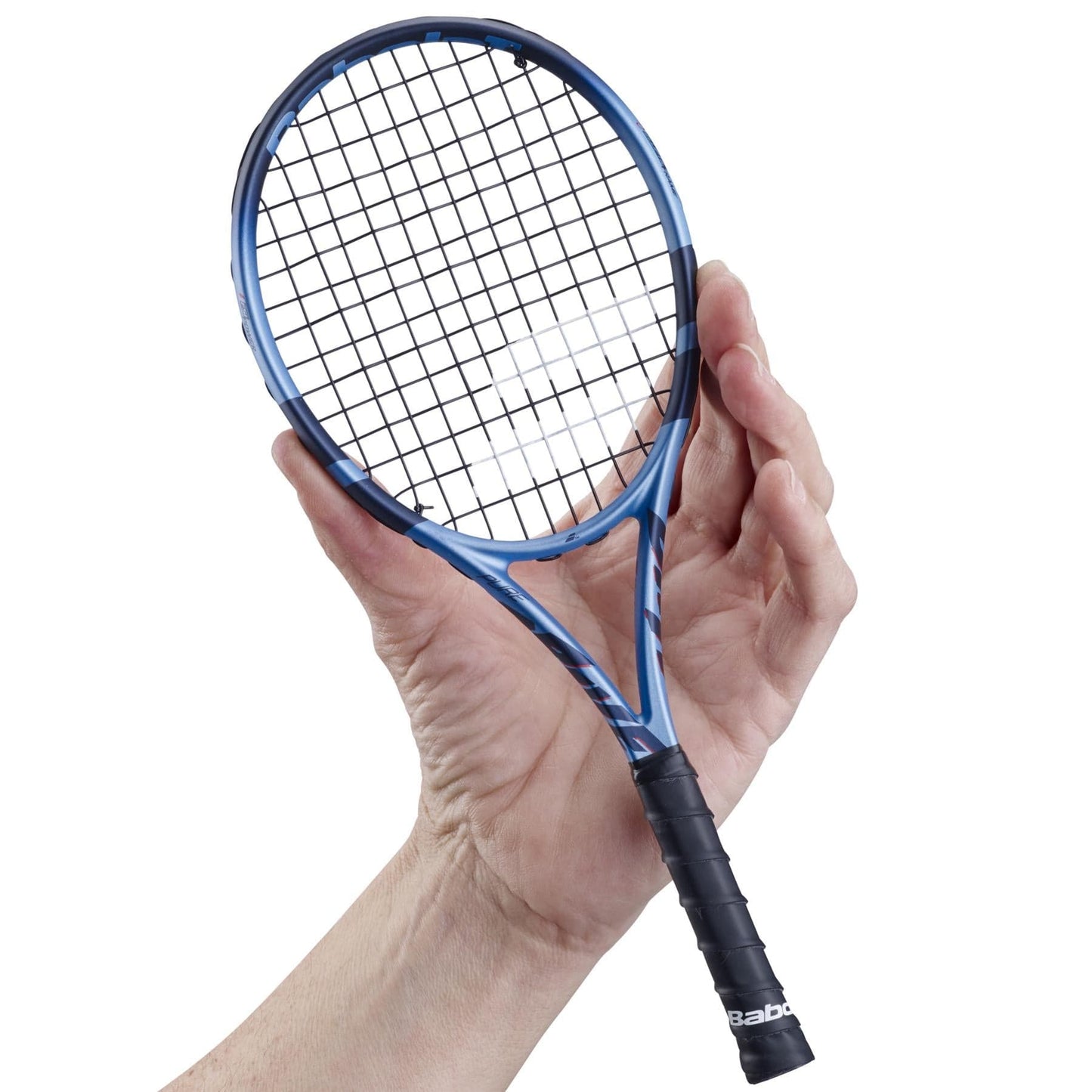 A hand holds a Babolat Mini Pure Drive 25 Tennis Racket, a small blue and black tennis keepsake with a black grip. The strings and frame are visible, and "Babolat" is printed on the handle against a plain white background.