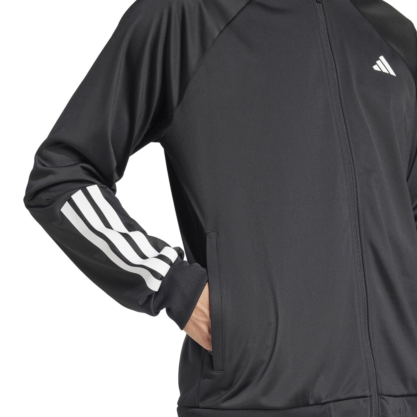 Someone in an ADIDAS Men's 3 Stripe Knit Tennis Jacket—black with white sleeve stripes and the iconic chest logo—stands with one hand in a pocket. A zipper closure is featured, but only part of the upper body is visible.