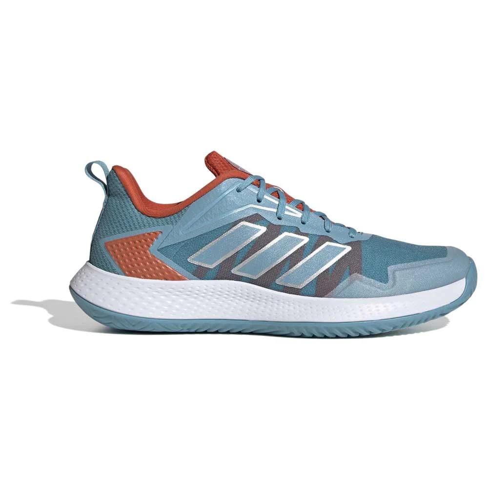 The adidas Defiant Speed Women's Tennis Shoes showcase a stylish athletic design in blue, complete with a white sole, an orange heel, and blue laces, all set against a white background. Constructed from recycled materials, these shoes feature unique geometric patterns and textured accents. The lightweight mesh upper ensures maximum comfort.