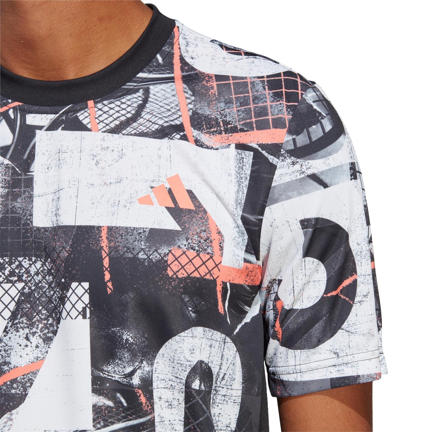 A close-up of someone donning the adidas Club Men's Graphic Tennis T-Shirt in white and black, highlighting an abstract design with graphic elements such as grids and lines. This shirt is crafted from recycled polyester and features AEROREADY moisture-wicking technology for a dynamic appearance.