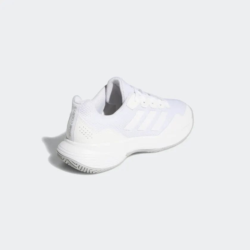 The adidas GameCourt 2 Women's Tennis Shoes in white are displayed at an upward angle, emphasizing their striped design and textured hard court outsole. The light gray background accentuates the sleek style of these shoes by adidas.