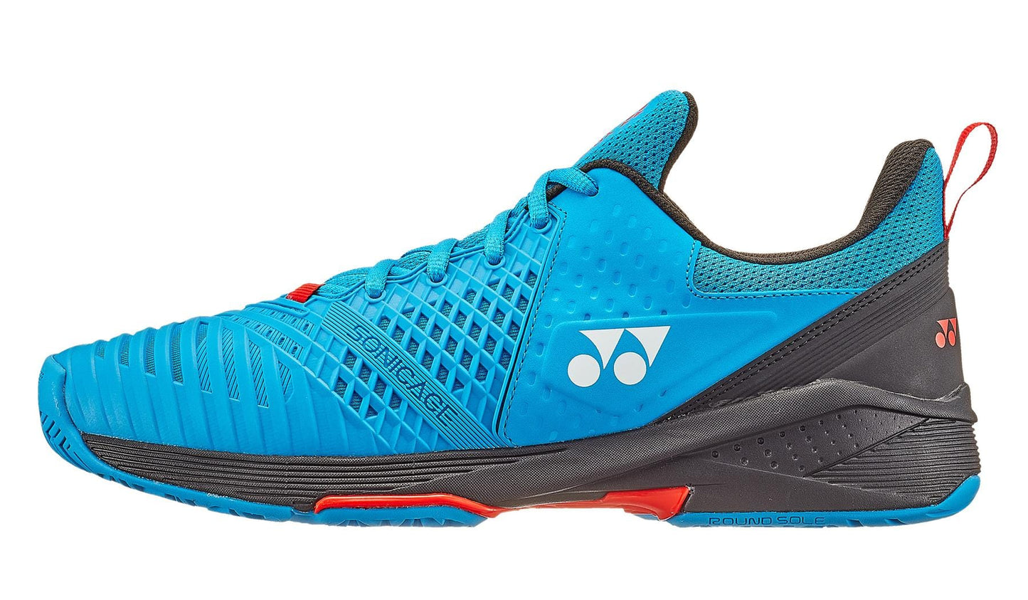 The Yonex Power Cushion Sonicage 3 Wide Men's Tennis Shoes are a striking blue with a bold white logo on the side, complemented by light blue laces and black and gray accents. The soles feature eye-catching red details. Crafted for performance, these shoes include a textured design and a convenient back loop for easy wear, making them ideal tennis shoes equipped with Yonex's Power Cushion technology.