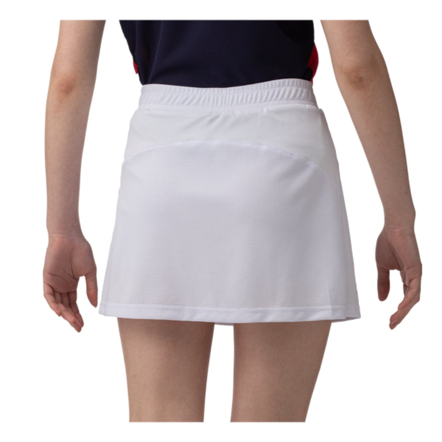Rear view of a person wearing a navy top and the Yonex 26094 Women's Skort - White, standing against a plain background. This skort by Yonex showcases subtle texture with an elastic waistband and is designed with VERY COOL technology that offers UV reduction. The person's arms rest naturally at their sides.