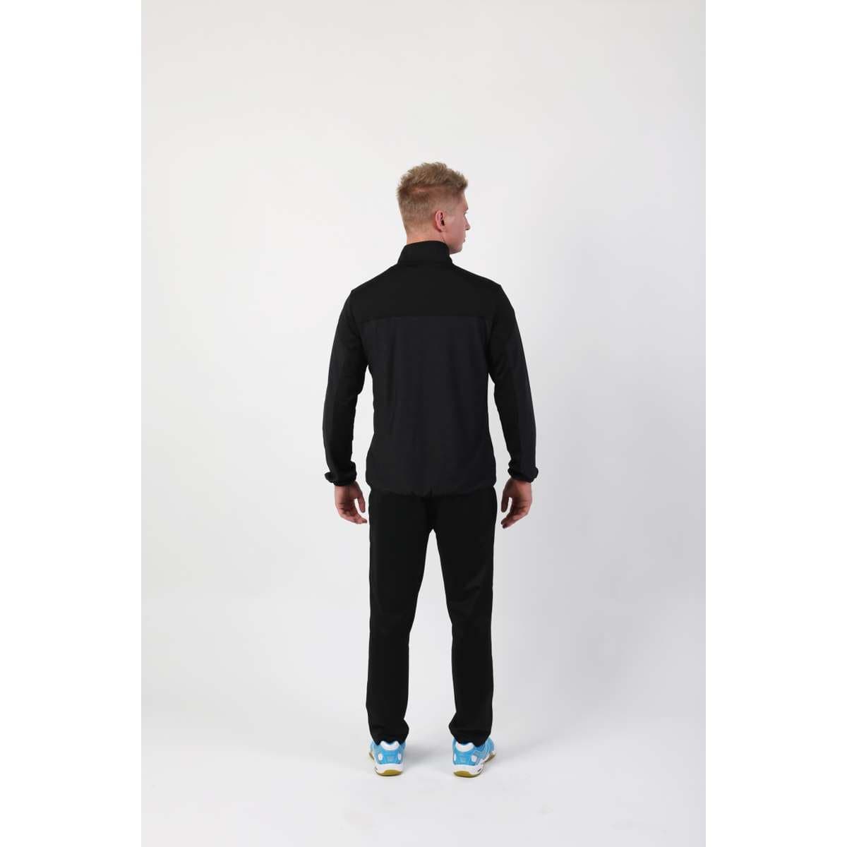 A person wearing the FZ Forza Bradford Jacket in black and blue sneakers is standing with their back to the camera against a plain white background, prepared for upcoming tournaments.
