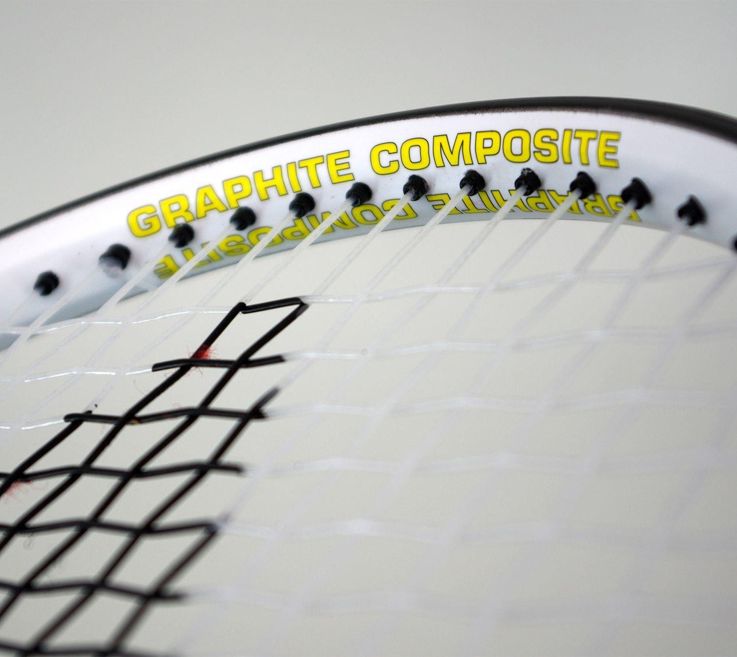 Close-up of a Karakal Pro Composite Tennis Racket - Black / White, featuring "Graphite Composite" printed in yellow on the frame. The tightly woven strings highlight its graphite composite construction, making it perfect for beginner to intermediate players.