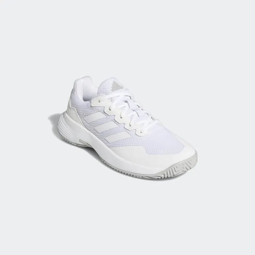 The adidas GameCourt 2 Women's Tennis Shoes in white are styled like traditional tennis footwear, showcasing a mesh upper, textured sole, and lace-up design. The recognizable GameCourt 2 logo by adidas is prominently displayed on the side of the shoe, and it is presented against a light gray backdrop in the photograph.