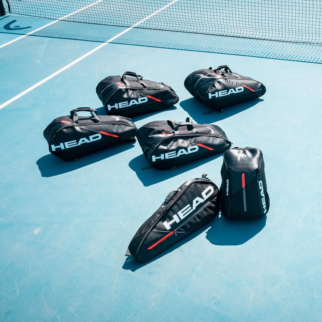 Six HEAD Tour Team 3R Tennis Bags in black and mint, featuring white "HEAD" branding, are arranged on a blue tennis court. Each bag includes an adjustable shoulder strap, with a net visible in the background.