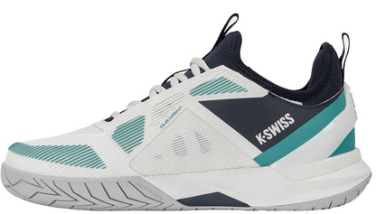 The K-Swiss K-Frame Speed Rublo Men's Tennis Shoes in White, Carbon, and Baltic feature athletic styling with teal and navy accents, a textured sole, and prominent "K-Swiss" branding on the side. The design includes mesh panels for breathability, plus a black tongue and collar. These shoes incorporate the signature K-Frame support technology—favored by pros like Andrey Rublev—for enhanced stability on the court.
